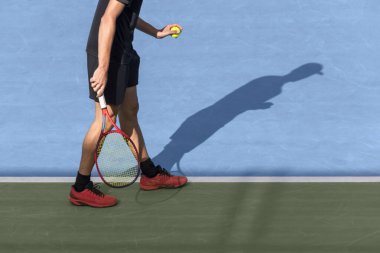 Elinde top olan tenisçi maçın başında servis yapmaya hazır. Genç erkek atlet mavi sert kortta tenis oynuyor. Kopya alanı olan spor arkaplanı