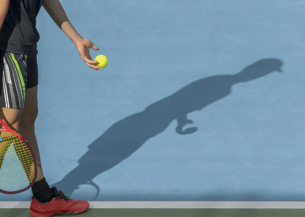 Young tennis player with ball and racket performs serve while playing on red clay court. Tennis game, match, tournament concept. Sport background, shadow, copy space