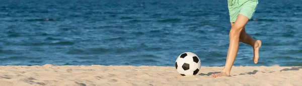 Garoto Joga Bola De Futebol Na Praia Arenosa. Pés Descalços De