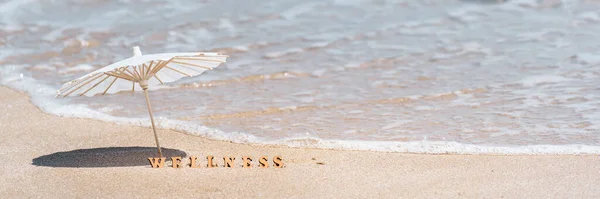 Summer holiday or vacation at sea wellness spa resort concept. Word wellness and beach umbrella on sand and blue sea in background. Banner, copy space