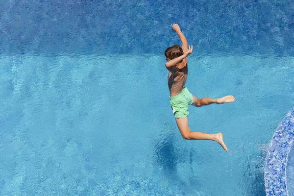 10 year old boy jumping into water in pool, having fun in summer vacation at hotel in health resort. Water sports and games, summer holiday concept.