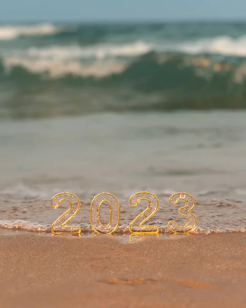 Numbers 2023 on golden sand of beach and blurry sea wave at sunrise or sunset. New Year's Eve travel, vision, dreams, goals concept. New year holidays greeting card.