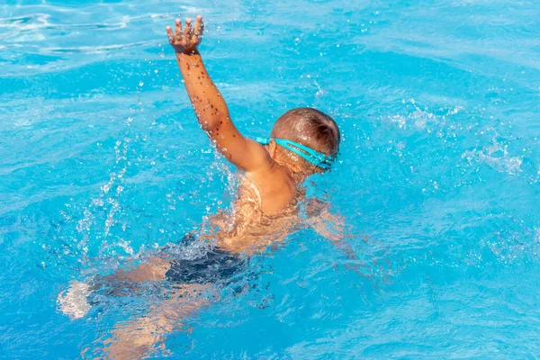 Little boy beginner swimmer learn to swim in pool crawl. Kid swimming in the water pool. Swimming lessons and water safety education for children