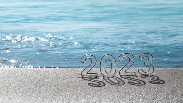 Happy new year 2023 wide banner, background. Numbers 2023 on sand of beach and blurry blue sea. New Year\'s Eve holidays celebration, travel, vision, dreams, goals concept, copy space