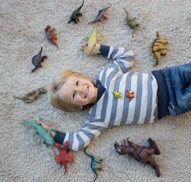 Tatlı çocuk sırtındaki hafif halıda yatıyor. Etrafına yayılmış bir sürü dinozor figürü var. Küçük bilim adamı, çocukların hobisi, tarih öncesi hayvanlar. Çocuklar için ilginç oyunlar. Eğlenceli çocukluk
