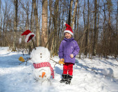 chlapec 4 - 5 let v Santa klobouk stojí v lese vedle domácí legrační sněhulák obrátil vzhůru nohama. Vánoční sváteční období v zasněženém lese. Zimní procházky a zábava se sněhem. šťastné dětství