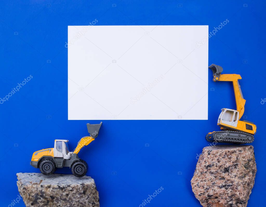 white blank paper for advertising lettering between small toy construction excavator and loader. business - congratulations, day of the builder. Advertising for the construction business