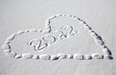 Karda, ayakkabı izlerinden yapılmış bir kalbin sembolik çizimi. 2022 yılının rakamları kalbin içinde yazılı. Karda ayak izleri. Noel arifesi, yürüyüş eğlencesi, kış tatili