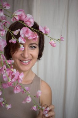 Güzel bir kadın elinde dallarla bahar pembesi çiçekleriyle büyüleyici bir şekilde gülümsüyor. Bahar atmosferi pozitif ruh hali, dikkatsizlik, geleceğe güven, kadınlık. seçici odak