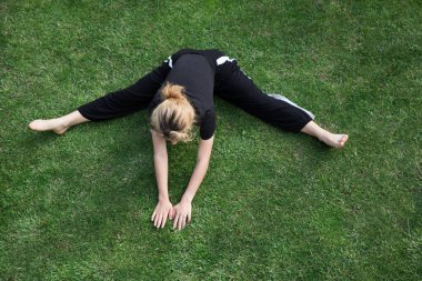 Genç bir kadın yeşil çimlerin üzerinde uzanırken esneme egzersizleri yapıyor. Aktif yaşam tarzı, huzur içinde yat. Yukarıdan görüntüle
