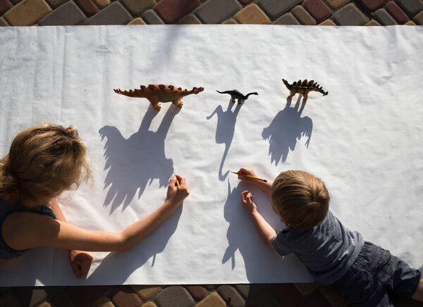 adult and a child draw contrasting shadows from toy dinosaurs. ideas for children's creativity. Interesting creative activities for children at home and in kindergarten. View from above.