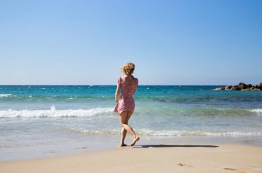 yaz tatilleri boyunca sahil boyunca kısa elbiseli, tanınmayacak kadar zayıf genç bir kadın sahilde yürüyor. Rüya gibi, güzel denize bak, fanteziler, ilham, doğanın enerjisi.