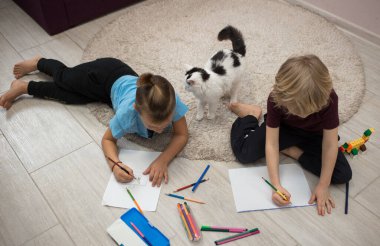 İki anaokulu öğrencisi, kardeş ya da arkadaş, çocuk odasının zeminine kurşun kalemle resim çiziyorlar. Eğitici oyunlar, çocuklar için günlük ilginç aktiviteler. Evde rahat bir gün. Üst görünüm