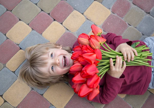 Vidám Nevető Ötéves Fiú Egy Csokor Vörös Tulipánnal Járdán Fekszik — Stock Fotó