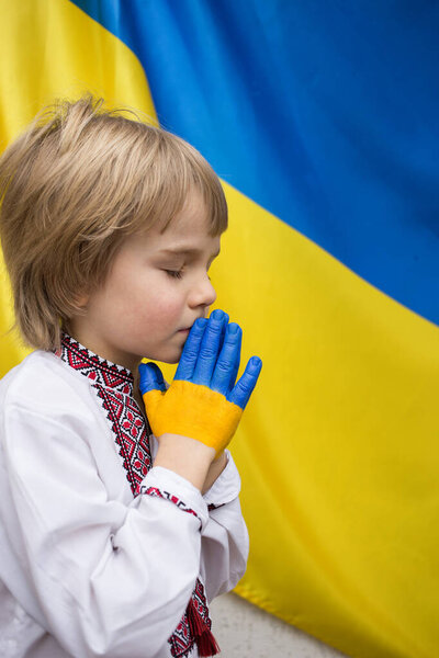 Дети против войны. Вторжение России на Украину, просьба о помощи мирового сообщества. Ребенок на фоне украинского флага с раскрашенными в желто-синий цвет руками, жест веры и надежды