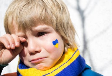 face of a frightened boy, a painted heart on the cheek in yellow-blue colors of the Ukrainian flag. Russia's invasion of Ukraine, a request for help to the world community. Children ask for peace clipart
