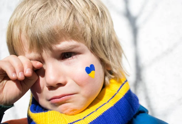 face of a frightened boy, a painted heart on the cheek in yellow-blue colors of the Ukrainian flag. Russia\'s invasion of Ukraine, a request for help to the world community. Children ask for peace