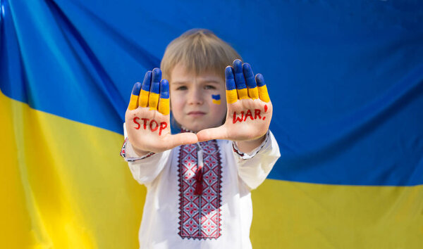 Boy in national Ukrainian clothes put his hands forward, inscription STOP War against background of yellow-blue flag. Russia's invasion of Ukraine, Children against war. War with Russia.