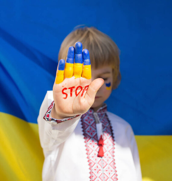 Against background of Ukrainian flag, child's hand, painted in yellow- blue, has inscription STOP. Russia's invasion of Ukraine, Children against war. Military conflict with Russia. Stay with Ukraine