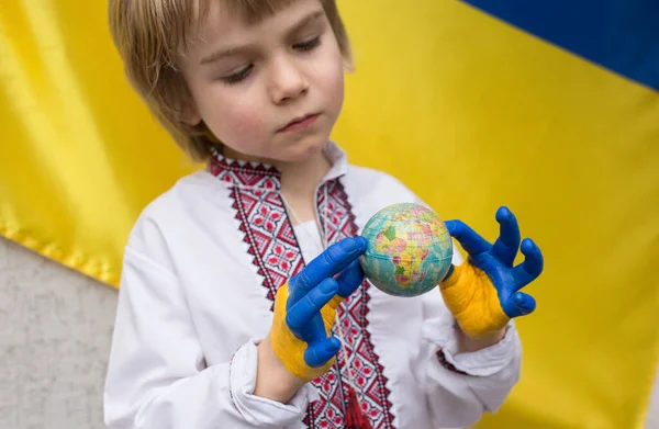 child in national clothes holds small globe ball. Children\'s hands painted in colors of Ukrainian flag. stop the war in Ukraine. national independence. Children against war. Stand with Ukraine