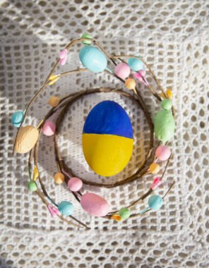 Tavuklu Paskalya yumurtası Ukrayna bayrağının sarı ve mavi renkleriyle beyaz örülü masa örtüsü üzerinde renklendirilmiştir. Savaş yok, Ukraynalılar barış istiyor. Destek, güvenlik, umut kavramı. Paskalya dekorasyonu fikirleri