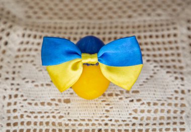 Ukrayna bayrağının sarı ve mavi renklerine boyanmış tavuklu Paskalya yumurtası beyaz örgü bir masa örtüsünün üzerinde saten bir fiyonk ile. Ukraynalılar barış istiyor. Destek, güvenlik, umut, inanç kavramı.