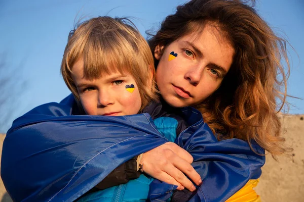 悲伤的男孩和一个年轻的女人 面颊上涂着蓝黄的国旗 在蓝天的映衬下 乌克兰人反对战争 与乌克兰站在一起 — 图库照片