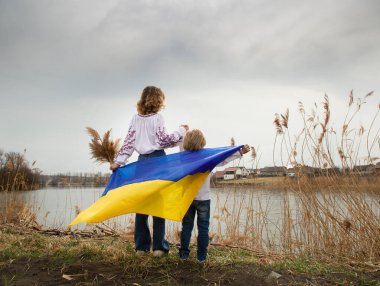 Küçük bir çocuk ve bir kadın, sırtlarını göl kıyısında mavi ve sarı Ukrayna bayrağıyla dikiliyorlar. Aile, mülteciler, birlik, destek, vatanseverlik. Ukraynalılar savaşa karşıdır. Ukrayna 'nın yanında dur