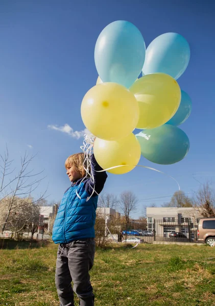 在一个阳光灿烂的日子里 学龄前男孩手里拿着一束黄蓝色气球 气球上有氦在天空中 支持乌克兰 乌克兰儿童反对战争 快乐的童年 — 图库照片