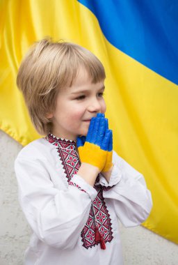 Çocuklar savaşa karşı. Çocuk, Ukrayna bayrağının arka planında elleri sarı ve maviyle boyanmış, inanç ve umut dolu bir jest. Ukraynalılardan dünya toplumundan yardım çağrısı