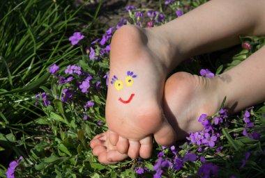 cute smiling face is drawn on the children's bare feet lying among the flowers. joy, cheerful positive atmosphere, happy childhood. Hello summer, day of smiles. Humor, prank