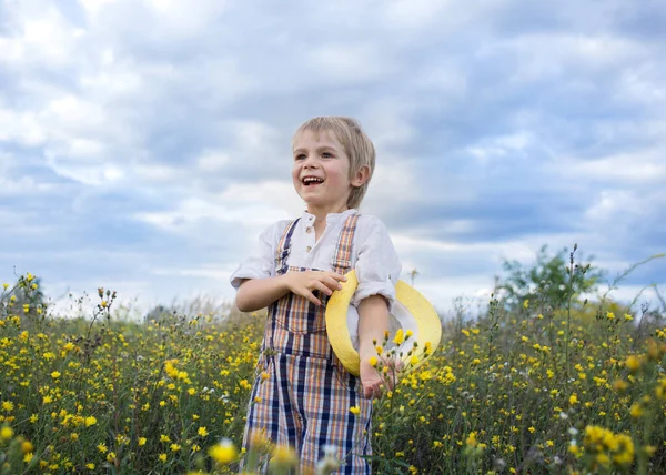 cute enthusiastic cheerful boy dressed in a rustic style stands in a field of wild yellow flowers. Summer mood, joyful childhood, spending time in nature. hello summer, feel happy