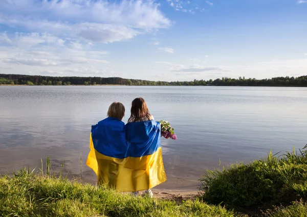 children stand with their backs on the shore of a lake with a blue-yellow Ukrainian flag. Family, refugees, unity, support. Ukrainians are against the war. stand with Ukraine