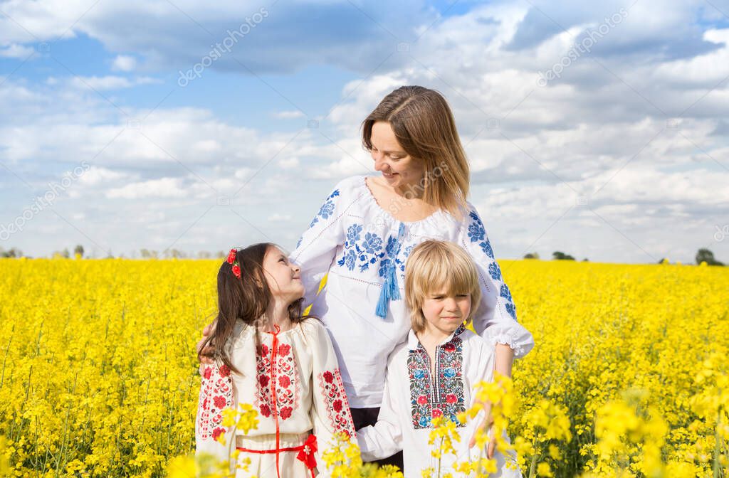happy Ukrainian family - mother, son and daughter in embroidered blouses stand among blooming yellow rapeseed field. Sunny day. unity, support. independence Day. Children of Ukraine ask for peace