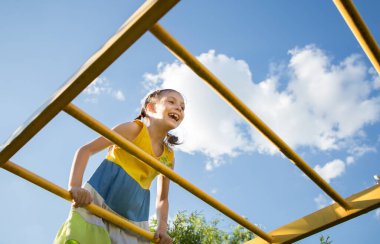 6-7 yaşlarındaki neşeli kız çocuk parkında. Çocukluk, dikkatsizlik, özgürlük, yaz tatili. Aşağıdan açı. Neşeli çocuğun yüzü gökyüzüne karşı