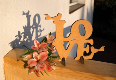 Işık duvarı arka planında - alstroemeria çiçekleri, ahşap bir yazı aşk ve kompozisyonun gölgeleri. Parlak güneşli bir gün. Sevgililer Günü konsepti. Işık ve gölge. Sevdiğin biri için sürpriz.