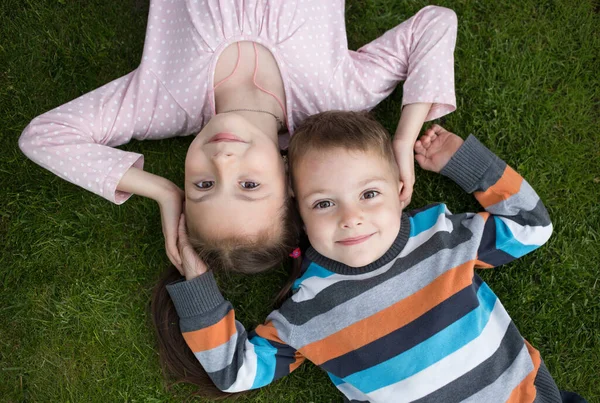 cute smiling older sister 7 years old and younger brother 3 years old lie side by side on the grass, look up. concept of happy childhood, friendly tender relations between the offspring in the family