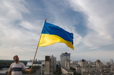 Ukrayna bayrağı, binaların yukarısındaki Kyiv 'deki bir evin çatısında duran bir adamın elinde. Ulusal özgürlük ve bağımsızlık sembolü. Savaşı durdurun. Dayanışma, zafer beklentisi, inanç
