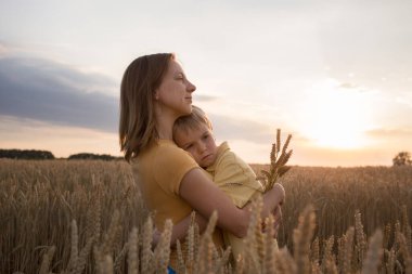 sad little boy snuggled up to his mother among the wheat field at sunset. a woman holds a child in her arms. Family, motherhood, refugees, unity, support, nostalgia. stand with Ukraine