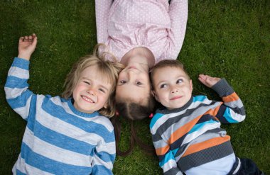 happy children, two boys and a girl lie on the grass with a sense of joy and unity. Good mood, carefree joyful childhood, friendship. view from above