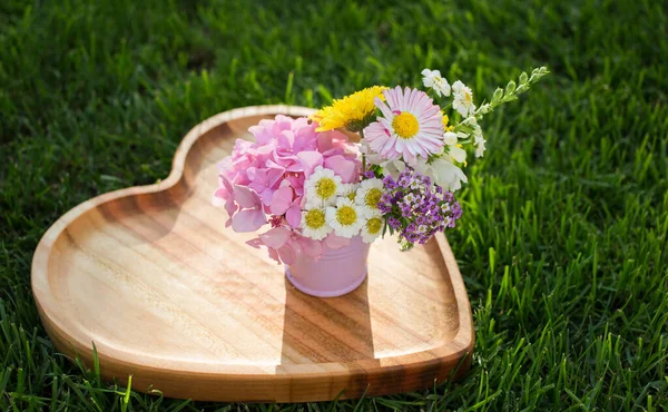 mini flower bouquet of various multi-colored flowers in a small metal bucket stands on a heart-shaped wooden board. Hello summer. Congratulation, declaration of love, positive thinking