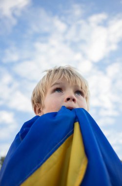 eyes of child look at sky, face is covered with Ukrainian flag. National symbol of freedom and independence. Russian invasion of Ukraine, Stop war. Hope and faith, children's fear and prayer
