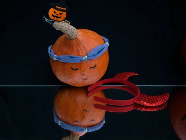 reflection in the mirror of an orange pumpkin with a woman\'s face, red decorative horns lie nearby. Transformation, fantasies, humor. Preparing for Halloween. selective focus.