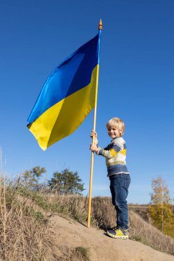 6 yaşında bir çocuk mavi gökyüzüne karşı mavi-sarı dalgalı bir Ukrayna bayrağıyla tepede duruyor. Ukraynalı olmaktan gurur duyuyorum. İnsanlar savaşa karşıdır. Ukrayna 'nın barışı, Ukrayna için barış kavramı