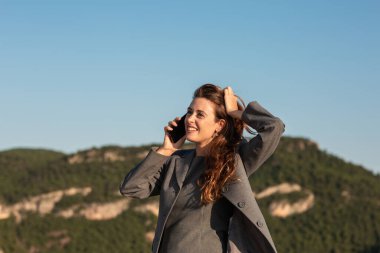 Doğada akıllı telefonla konuşan neşeli bir kadın.