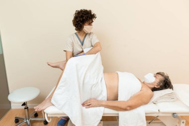 Fizyoterapist, havluları olan olgun bir kadına bacak masajı yapıyor.