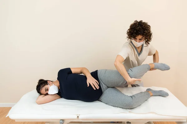 Fisioterapeuta masajeando piernas de mujeres embarazadas en el centro de salud —  Fotos de Stock