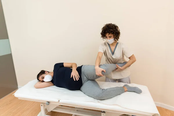 Fisioterapeuta masajeando piernas de mujeres embarazadas en el centro de salud —  Fotos de Stock