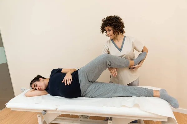Una mujer embarazada acostada sobre una camilla mientras un fisioterapeuta se masajea las piernas en un centro de salud. —  Fotos de Stock