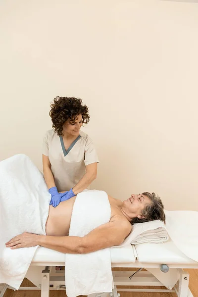 Side view of a physiotherapist checking diastasis recti on belly of mature woman — Stock Photo, Image